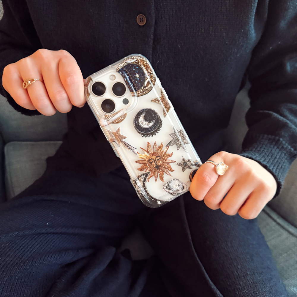 Clear phone case with gold sun, moon, and star designs held by person in black.