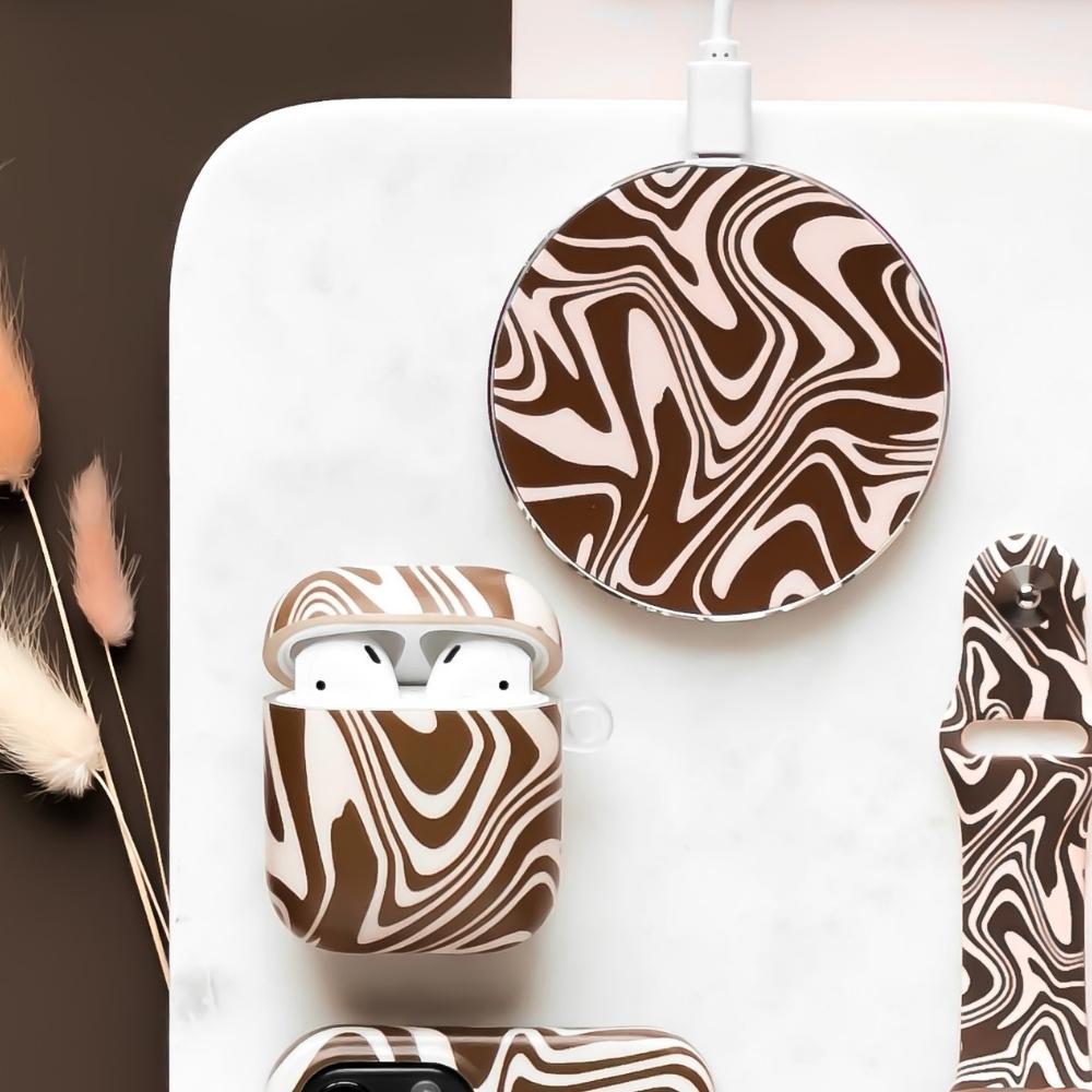 A stylish setup featuring a wireless charging pad, AirPods case, and phone case, all with a brown and white swirl pattern. Dried plants are arranged to the left, creating a modern and artistic aesthetic.