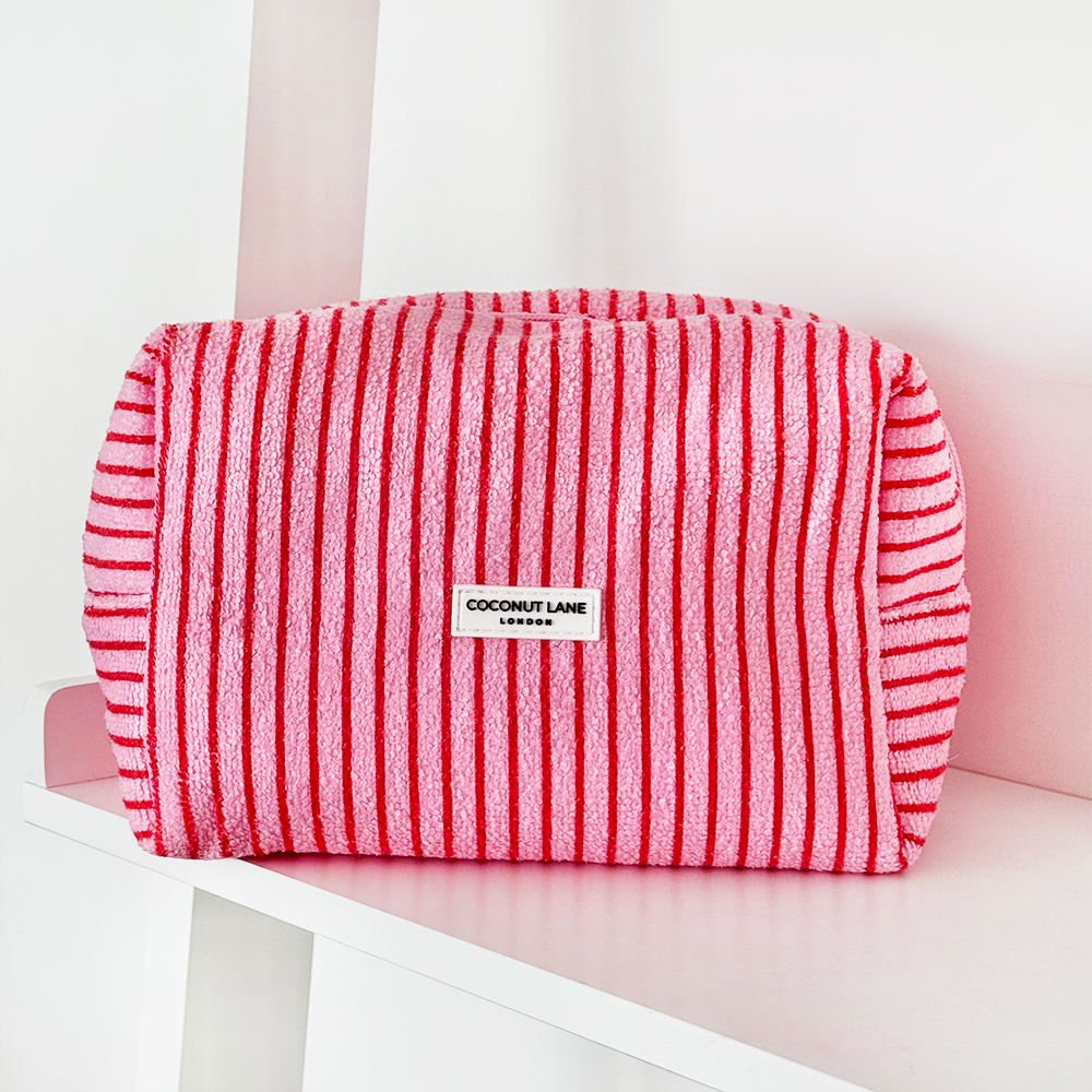 A pink and white striped toiletry bag with a zipper and a "Coconut Lane London" label sits on a white shelf.