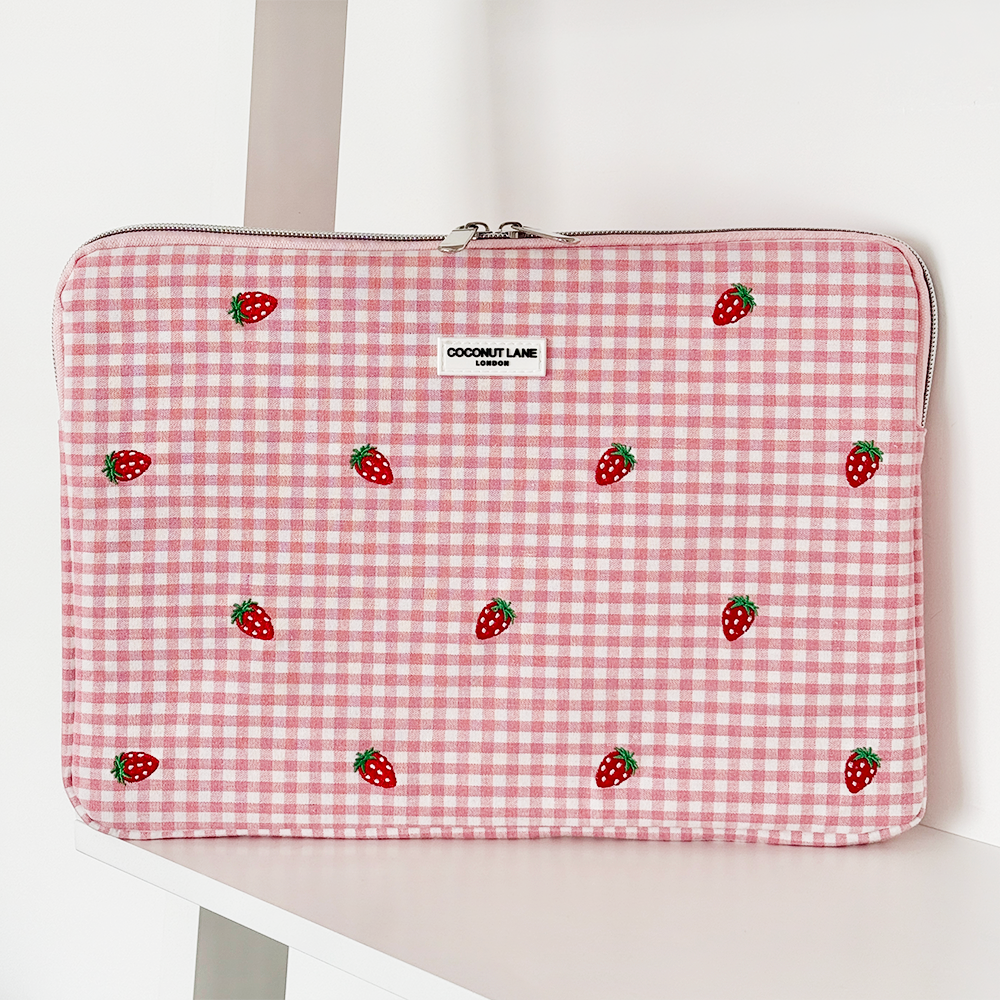 A quilted laptop sleeve with a floral pattern and a label that reads "COCONUT LANE" lays partially open on a white surface, revealing a glimpse of a laptop inside.