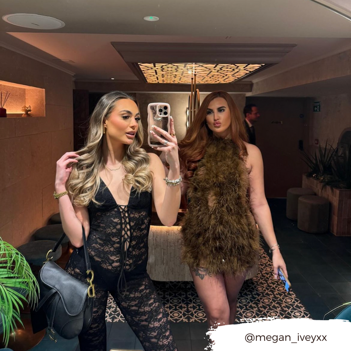 Two women are posing in a stylish, well-lit lobby area. The woman in front is taking a mirror selfie with her phone, which has a Coconut Lane Curvy Mirror Phone Case - Pink. She is wearing a black lace outfit and carrying a black handbag. The woman behind her is wearing a fur-like dress. Instagram handle @megan_iveyxx is overlaid.