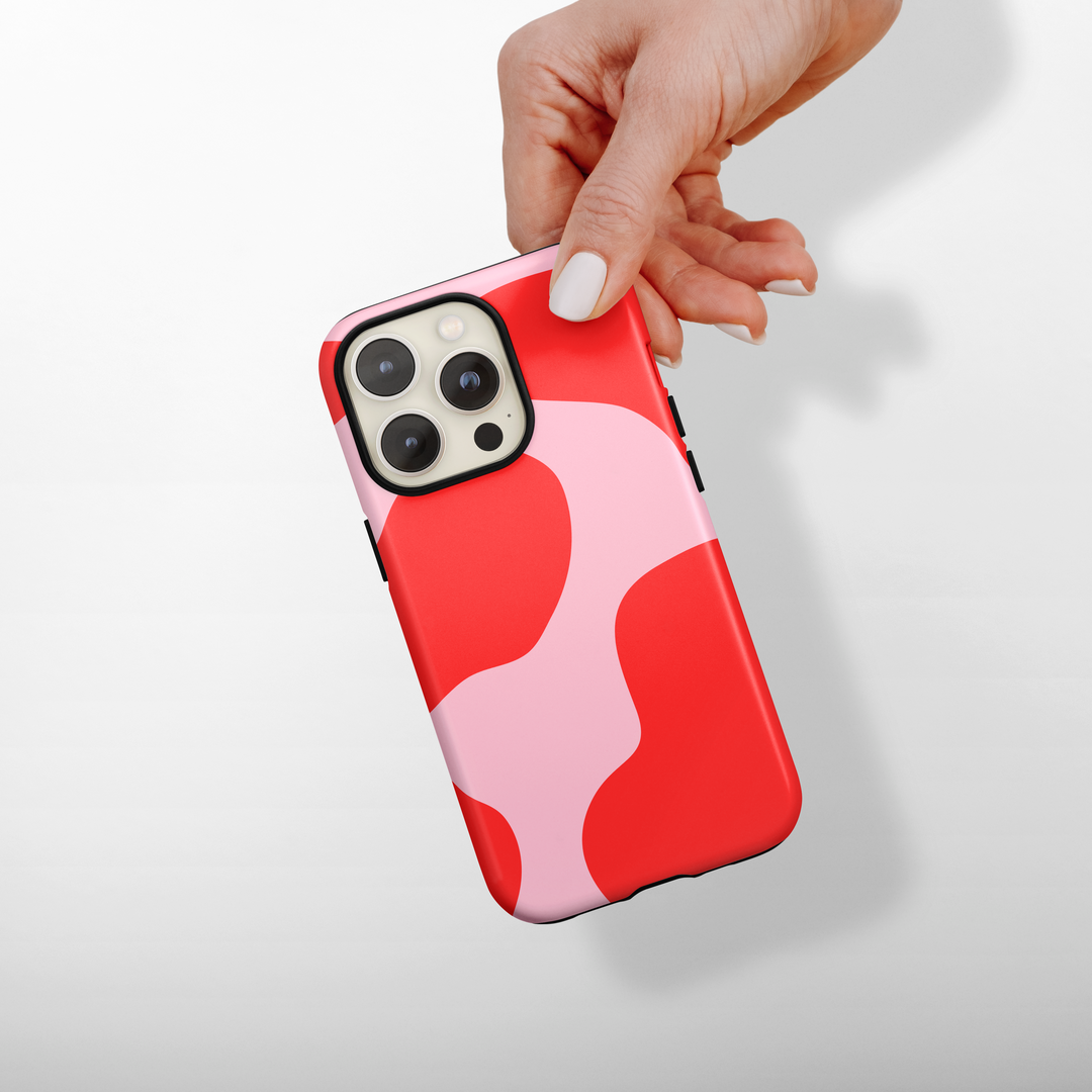 Hand holding a phone with a red and pink cow print case on a light gray background