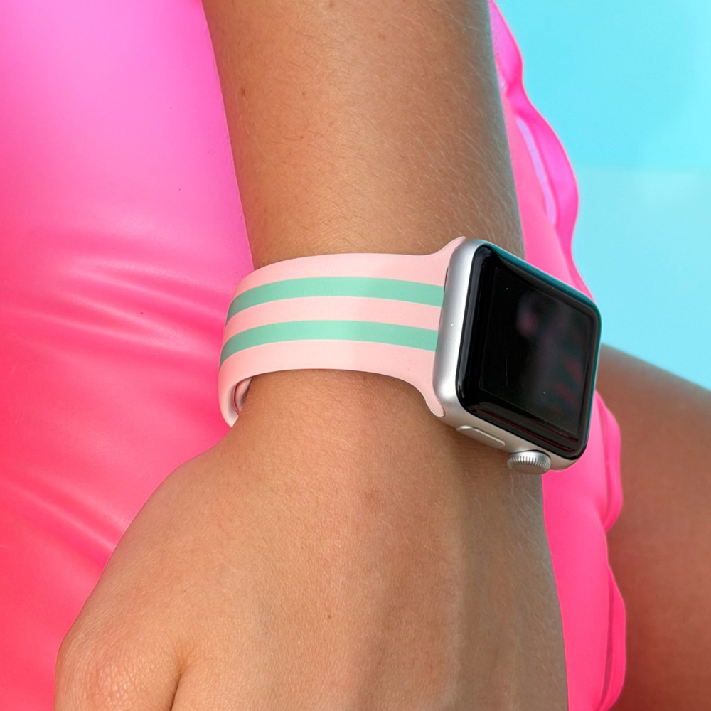 Apple Watch with a pink and green band on a person's wrist against a pink and blue background
