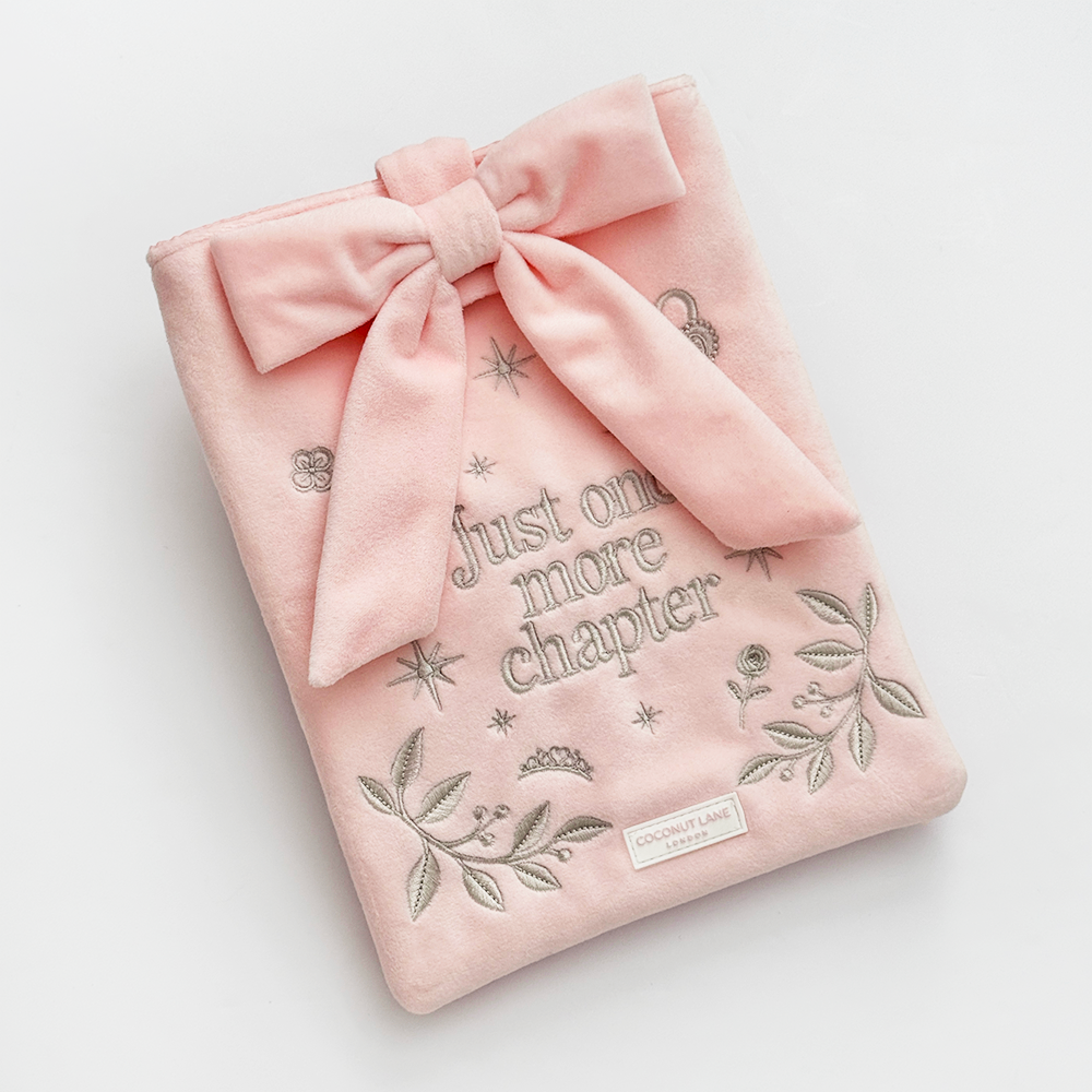 Book Sleeve made from soft blush pink velvet with grey embroidered floral details, stars and 'Just One More Chapter' lettering, finished with a large pink velvet bow and Coconut Lane logo, photographed on a white background.