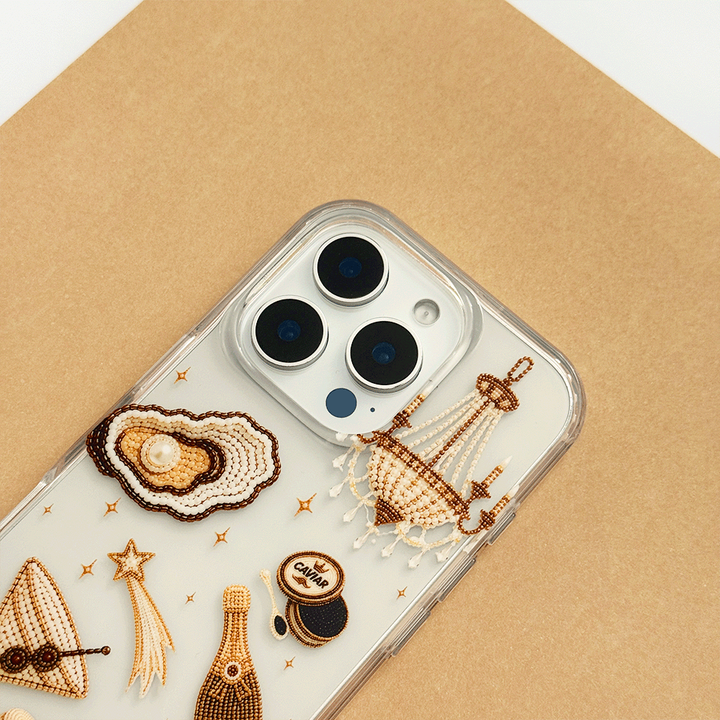 A clear phone case decorated with macron-style graphics of oysters, a cocktail, a champagne bottle, playing cards, and a macaron.