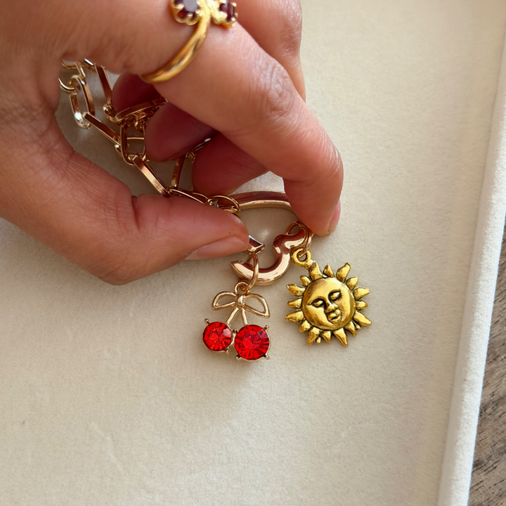 Gold Phone Strap Heart Clip with cherry and sun design held by a hand on a light background