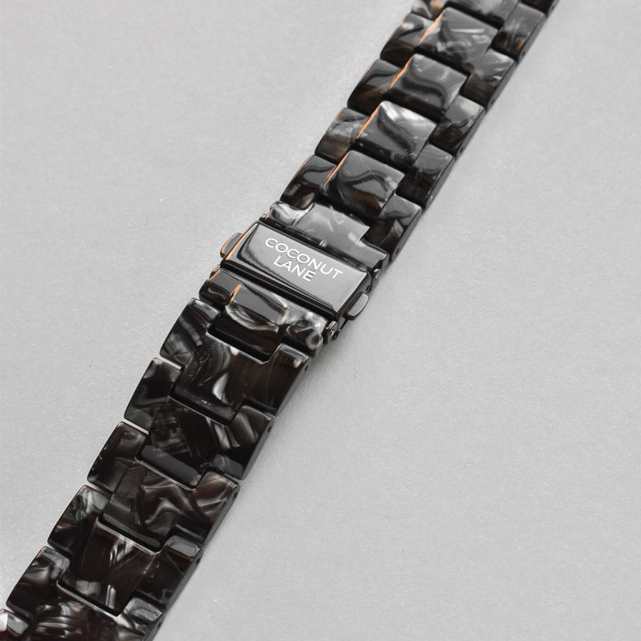 A stylish Luxe Black Marble Apple Watch Strap with a shiny finish is displayed against a light gray background. The metallic clasp, engraved with the brand name "Coconut Lane," enhances this chic accessory, perfect for elevating any outfit.