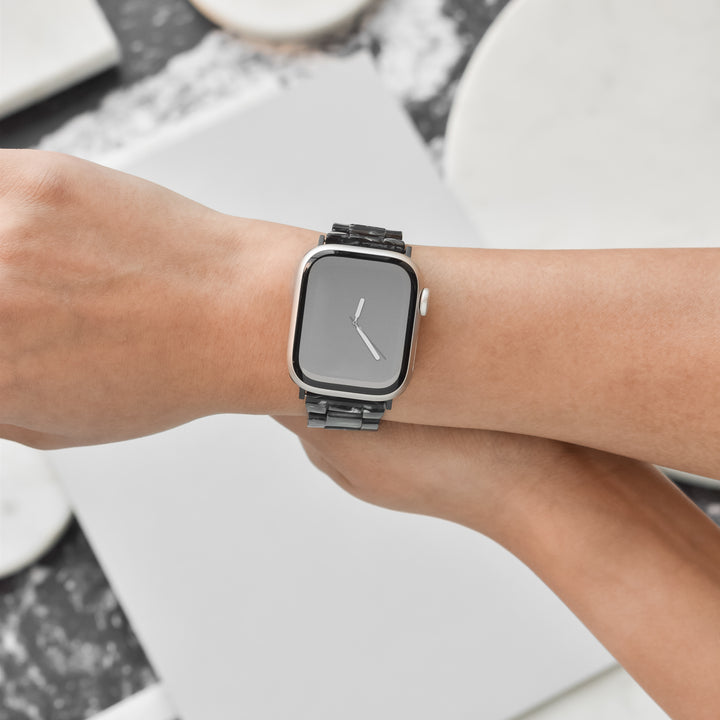 A close-up image of a person's wrist adorned with a sleek, modern smartwatch featuring a minimalist black rectangular face paired with the Luxe Black Marble Apple Watch Strap from Coconut Lane. The watch is elegantly displayed against a neutral background with Luxe Black Marble textures.