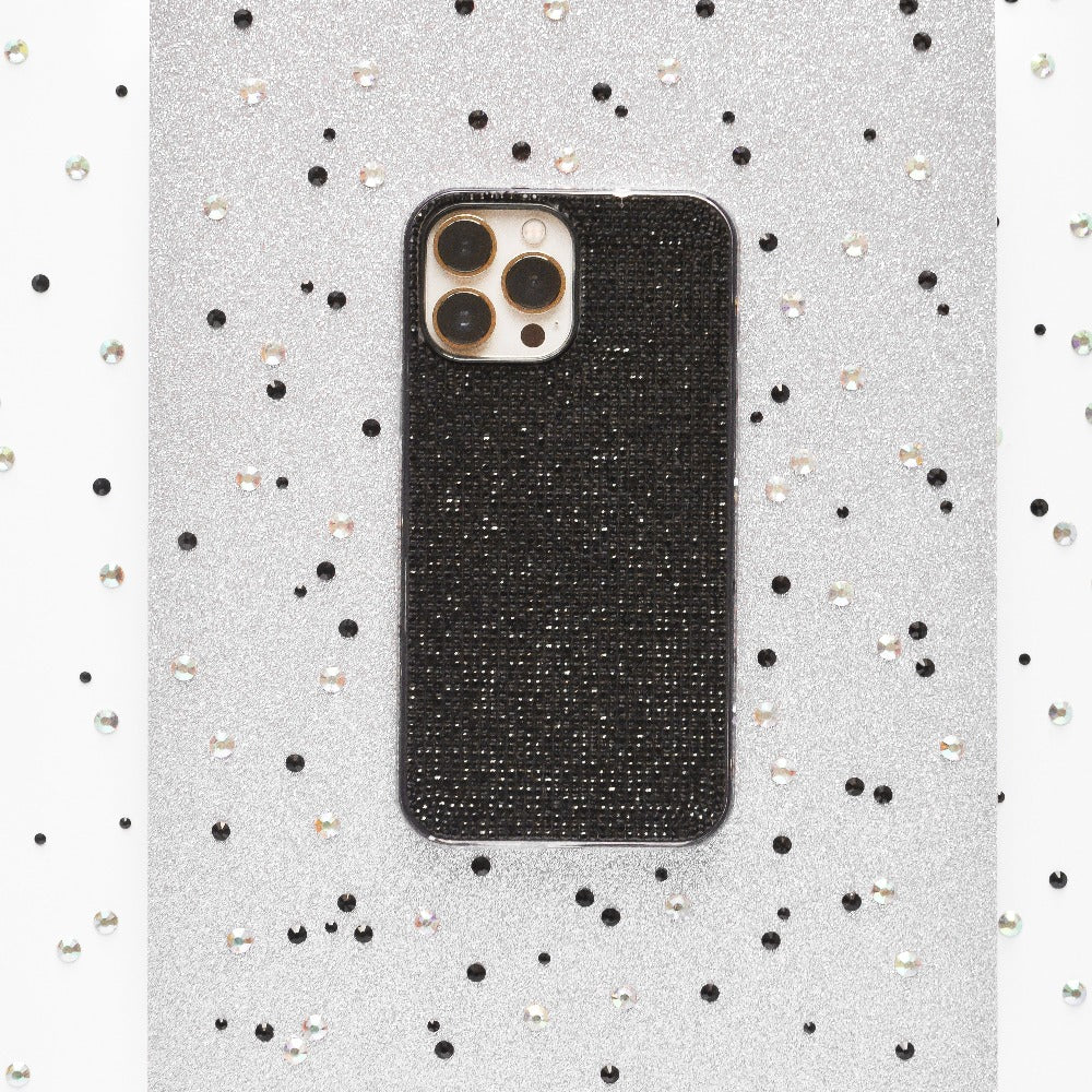 A black smartphone equipped with the Disco Sparkle Phone Case - Black by Coconut Lane is placed on a silver glittery background. The backdrop is adorned with scattered black and silver beads, enhancing the sparkle and texture of the scene.
