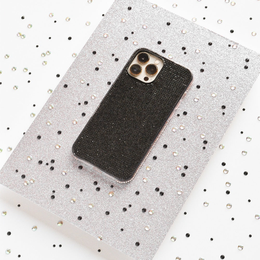 A smartphone with a Coconut Lane Disco Sparkle Phone Case - Black is placed on a silver glittery surface. The silver surface is adorned with scattered black and silver sequins, creating a festive and sparkly backdrop.