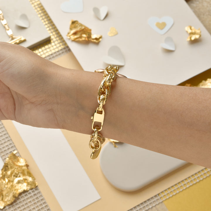 A wrist adorned with the Coconut Lane Chain Bracelet Apple Watch Strap in Gold, against a background featuring scattered gold foil pieces and white paper hearts. The surface underneath includes textured beige and white materials, creating a scene that evokes a sense of elegance and romance.