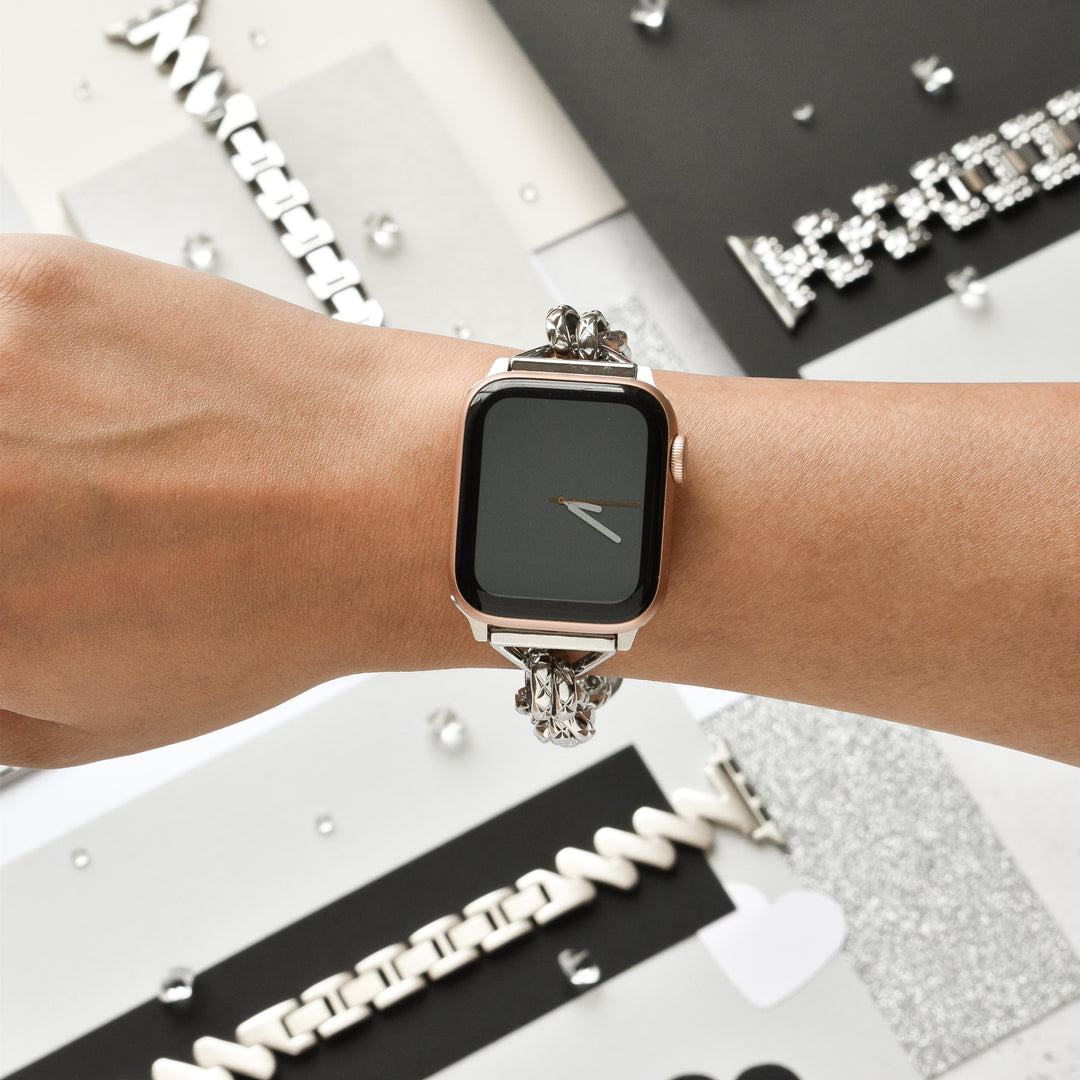 Close-up of the Chain Bracelet Apple Watch Strap - Silver by Coconut Lane on a person's wrist. The background features various stylish watch bands and metallic decorative elements, adding a sophisticated and modern aesthetic to the scene.