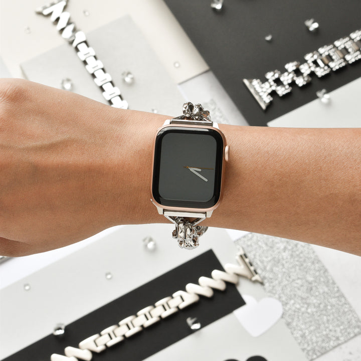 Close-up of the Chain Bracelet Apple Watch Strap - Silver by Coconut Lane on a person's wrist. The background features various stylish watch bands and metallic decorative elements, adding a sophisticated and modern aesthetic to the scene.