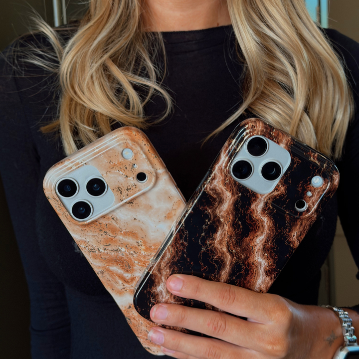 A woman holds two iPhone cases with a marble pattern. One case has a light beige and white marble design with subtle gold glitter flecks, and the other has a dark brown and black marble design with gold flecks.