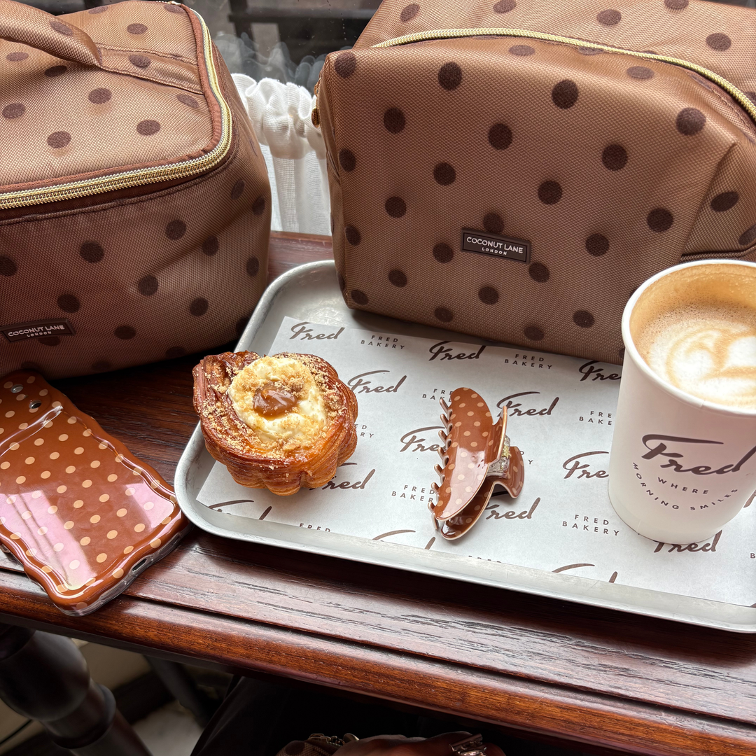 flat lay photo in a cafe, showing the Dot Society Chocolate Brown claw clip, alongside the matching makeup bag, wavy phone case and vanity case.