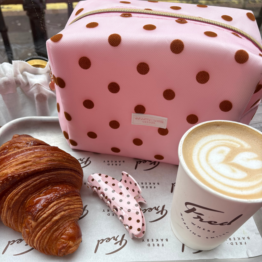 Flat lay photo in a cafe showing the Dot Society pink and brown collection. Including the pink and brown polka dot claw clip, with a matching makeup bag.