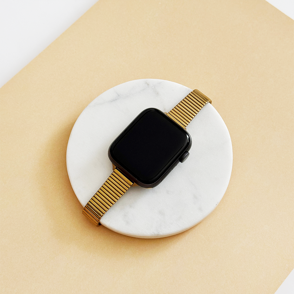 Gold Coconut Lane SLIM Fine Line Apple Watch strap on a black smartwatch, shown on a white marble surface.