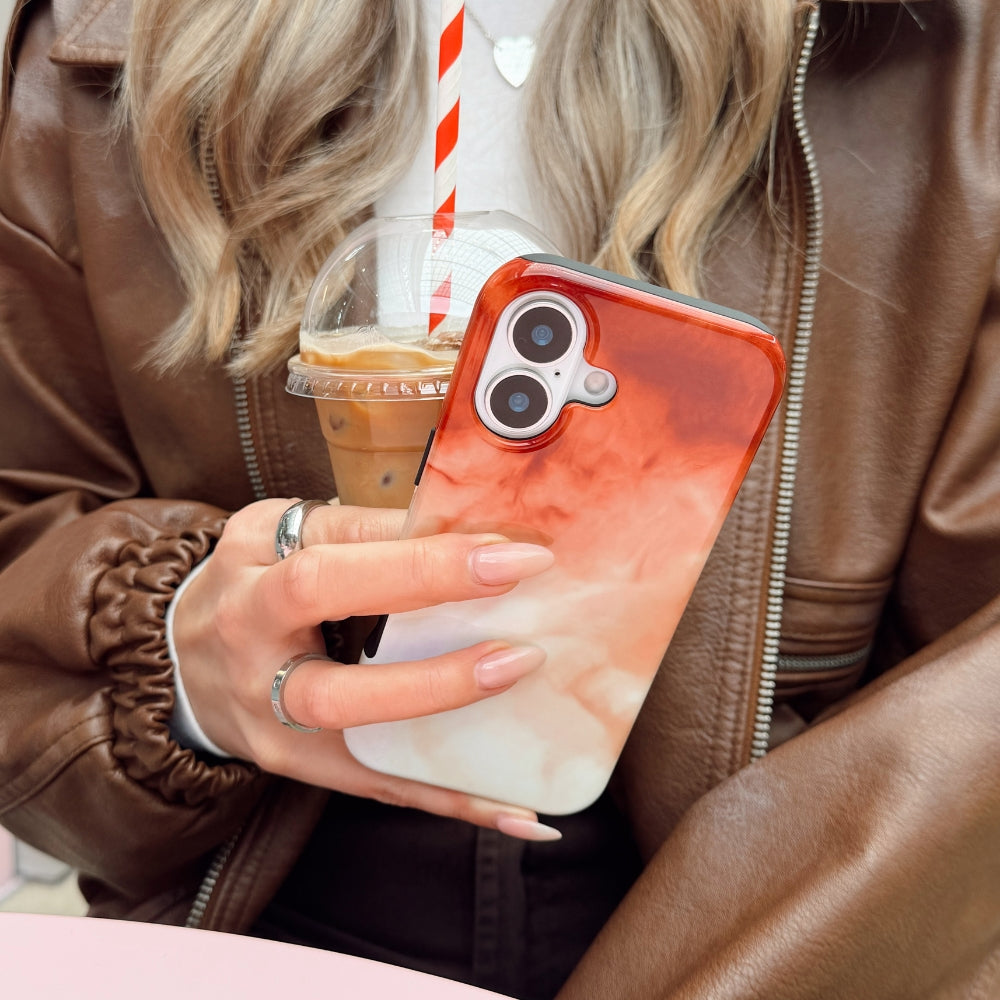 Girl holding a phone with an iced latte-inspired phone case and a drink, wearing a brown leather jacket.