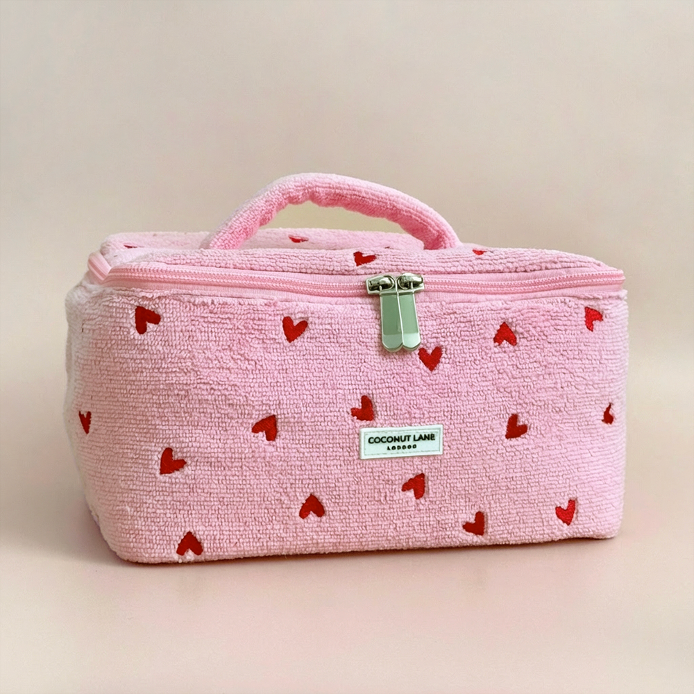 Pink cosmetic bag with red heart pattern on a beige background