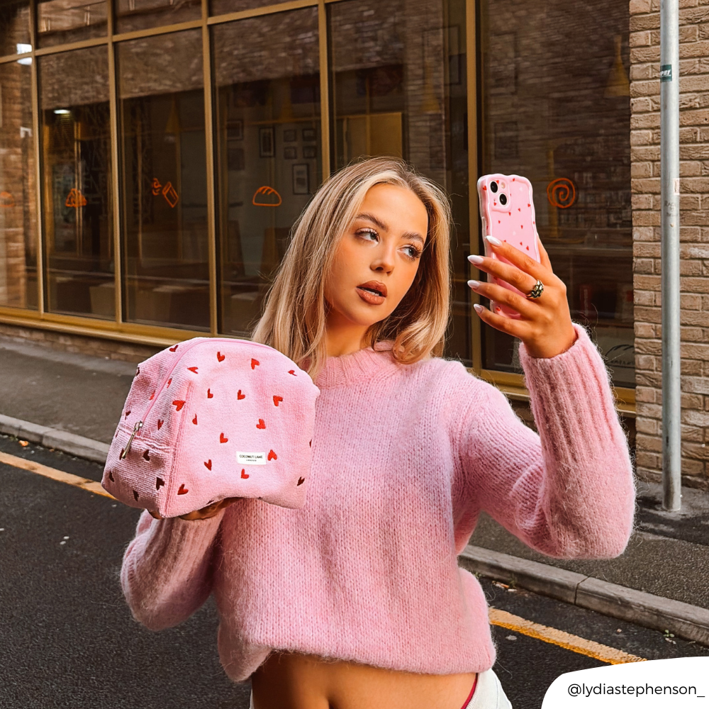 Girl taking selfie with cute hearts phone case whilst holding pink hearts makeup bag