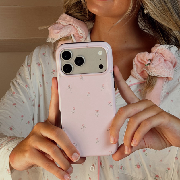 A woman takes a mirror selfie wearing a pink floral pyjamas and a pink pointelle heatless curls set. She holds a light pink phone case with a small floral pattern.