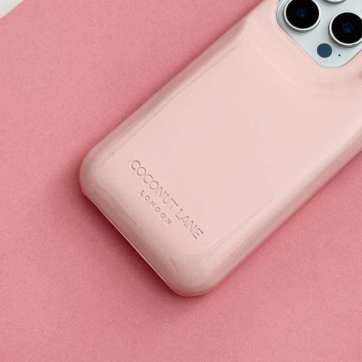 Close-up of glossy pastel pink Coconut Lane puffer phone case with embossed logo, displayed diagonally on a matching pink background.