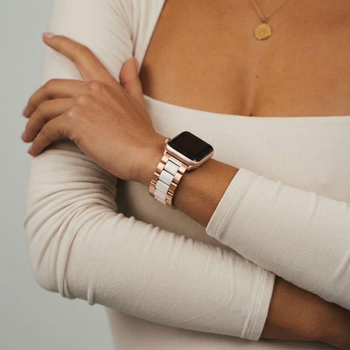 Person with arms crossed wearing a white and rose gold stainless steel Apple Watch strap and a gold necklace.