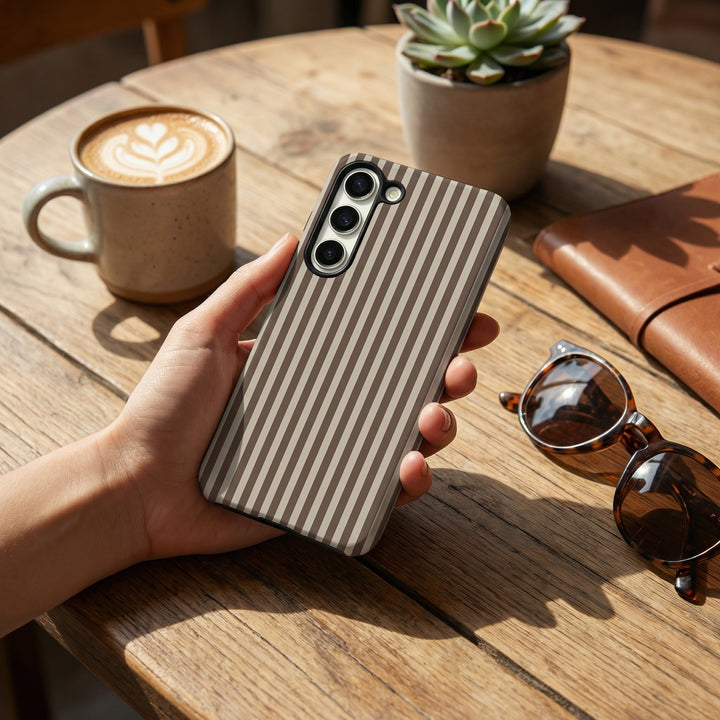 Brown and beige striped design Phone Case held in a hand, on a wooden table next to a cup of coffee and sunglasses.