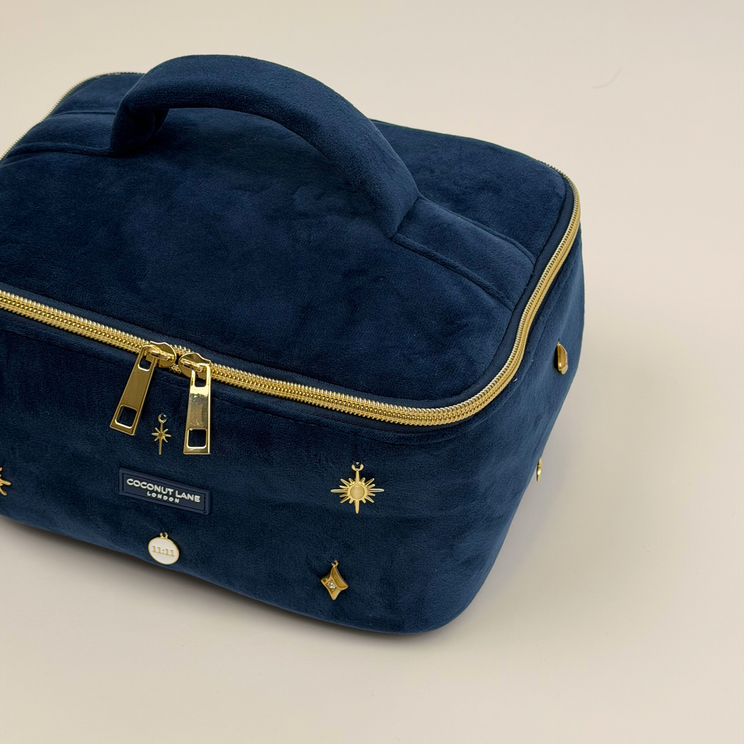 Stardust After Dark Vanity Case. A dark blue navy velvet vanity case with gold zip, and sewn-on gold celestial-themed charms. Including a moon, sun, star, diamond shape and 11:11 charm. 