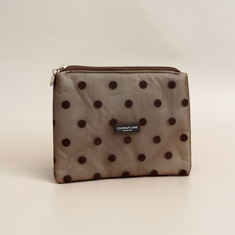 Brown mesh pouch with dark brown polka dots, a gold top zip with a heart-shaped zip pull, and a black Coconut Lane London logo badge on the front, shown on a beige background.