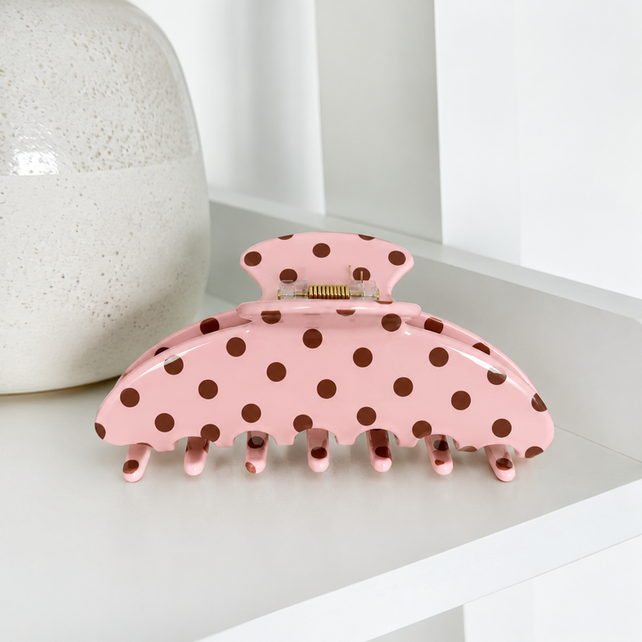 Coconut Lane pink and chocolate brown polka dot claw clip with a glossy finish, curved teeth and gold-tone spring, displayed on a white shelf.