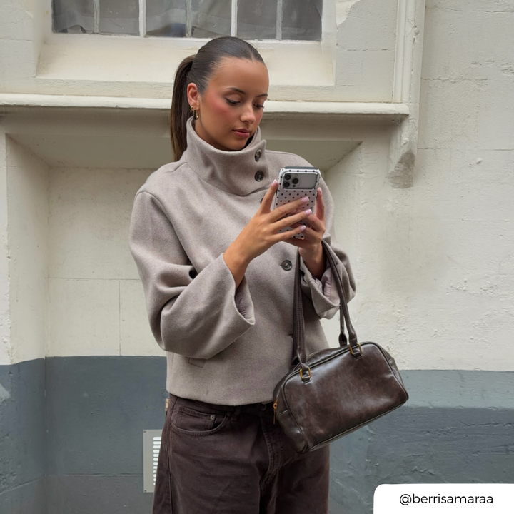 Woman with brunette hair tied in a ponytail holding an iphone in a cream and brown polka dot phone.