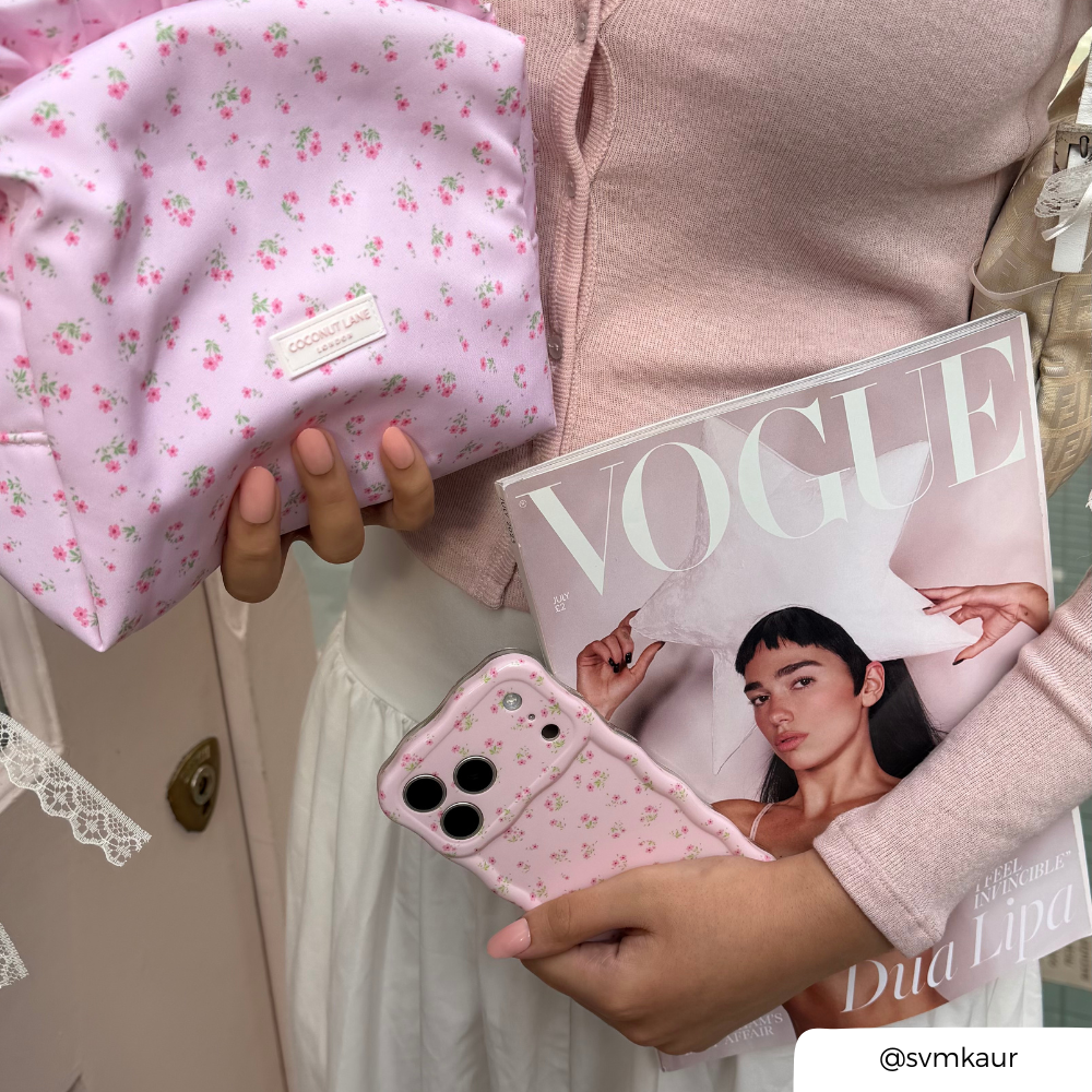 A person in a pink cardigan holds a light pink floral makeup bag pouch, a Vogue magazine, and a pink floral phone case with a wavy edge.
