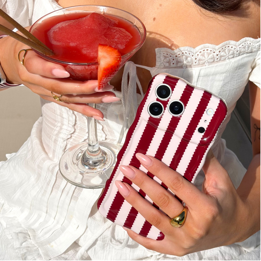 Girl sat on sun bed by pool holding her strawberry daiquiri next to her Wavy Blushberry Scallop Stripes Phone Case in a pink colour