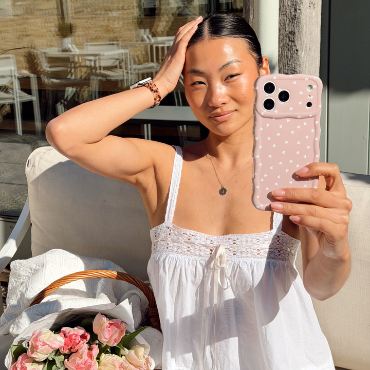 Girl posing with flowers in a basket holding the Wavy Chai Hearts Phone Case
