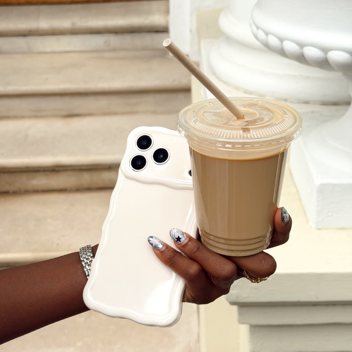 Girl holding her wavy phone case in cloud dancer next to her iced coffee