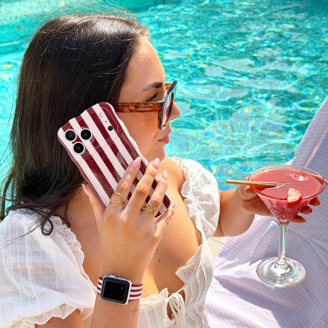 Woman lounging by a pool holding a the phone case, wearing a white dress.