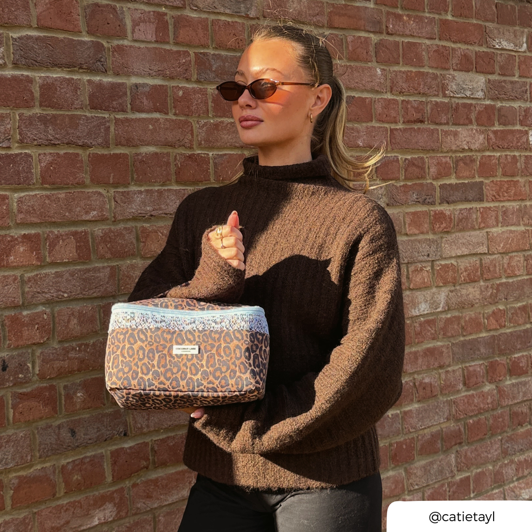 Woman in a brown knit jumper holding the Coconut Lane Leopard Lace vanity case featuring brown leopard print, pale blue lace trim.