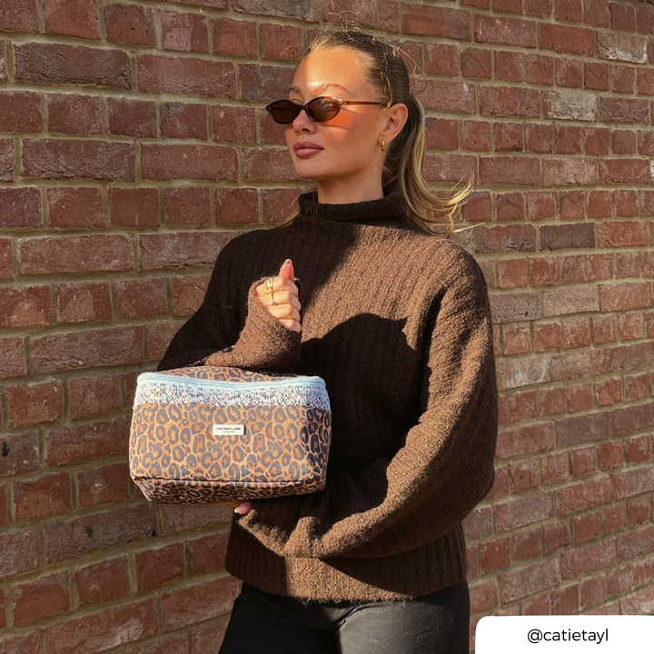 Woman in a brown knit jumper holding the Coconut Lane Leopard Lace vanity case featuring brown leopard print, pale blue lace trim.