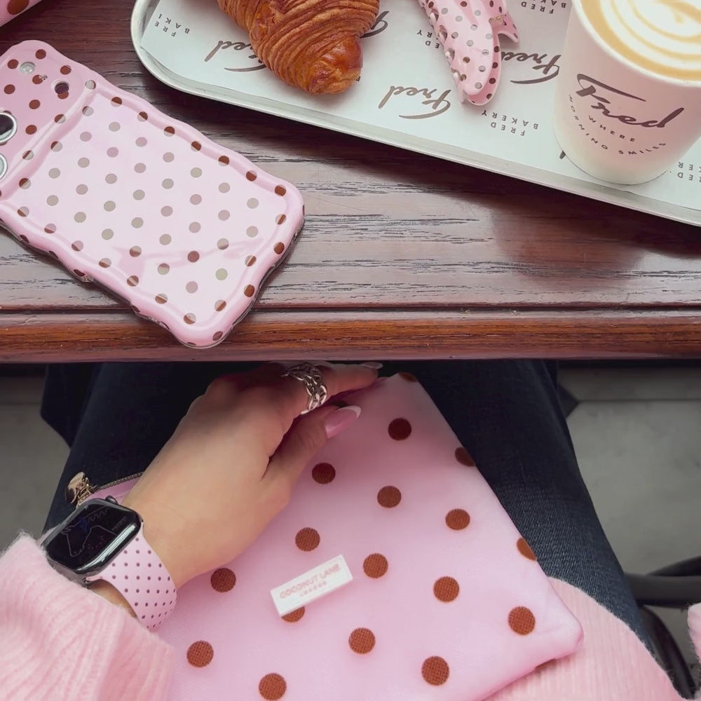 Dot Society Pink and Brown Everything Pouch. The pouch is sheer mesh material with brown polka dot detailing. Featuring in the photo is the matching Apple Watch Strap, pink with brown polka dots, alongside the matching wavy phone case.