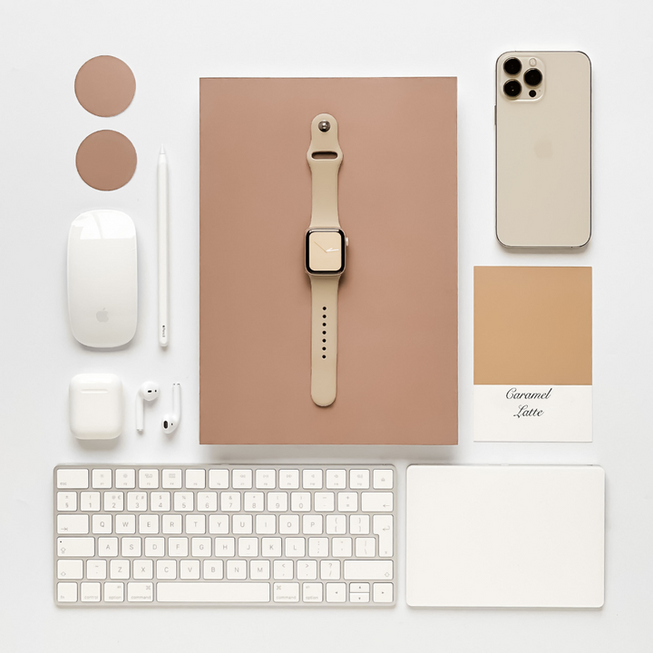 A neatly arranged flat lay featuring an Apple Watch with a Coconut Lane NAKD Apple Watch Strap - Caramel Latte, an iPhone, a stylus, a wireless mouse, a keyboard, AirPods, and a mouse pad from the NAKD Collection. All items are in neutral tones on a white background.