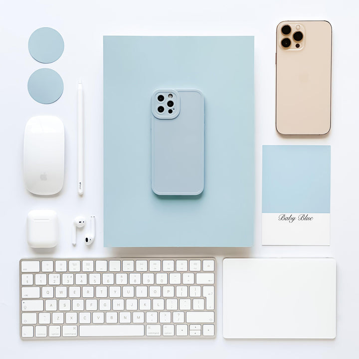 An organized flat lay features a beige smartphone, a blue smartphone with the NAKD Phone Case in Baby Blue by Coconut Lane, wireless earbuds, a stylus, a wireless mouse, a keyboard, a trackpad, and two round blue tokens. There's also a blue and white card labeled "Baby Blue." All items are arranged neatly on a white background.